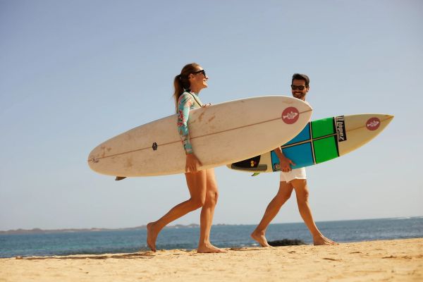 Pareja caminando por la playa con tablas de surf en Playa Esmeralda